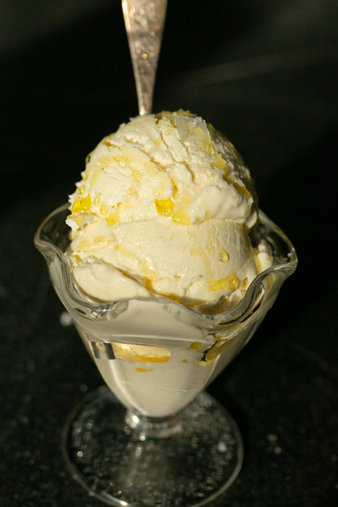 Glass sundae dish with a scoop of vanilla ice cream and oil drizzle on a dark background