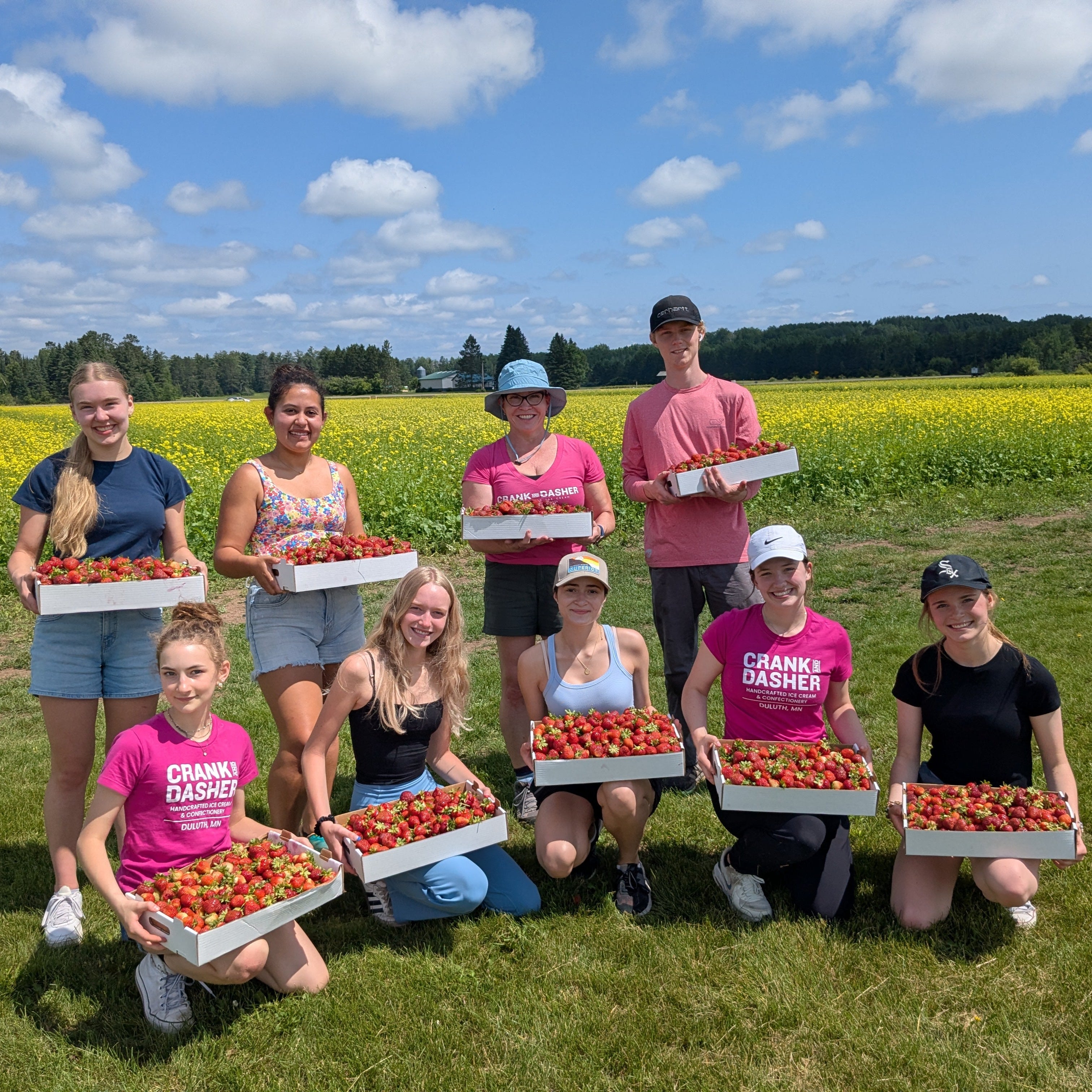 Group of people holding boxes of strawberries in a field with a blue sky.