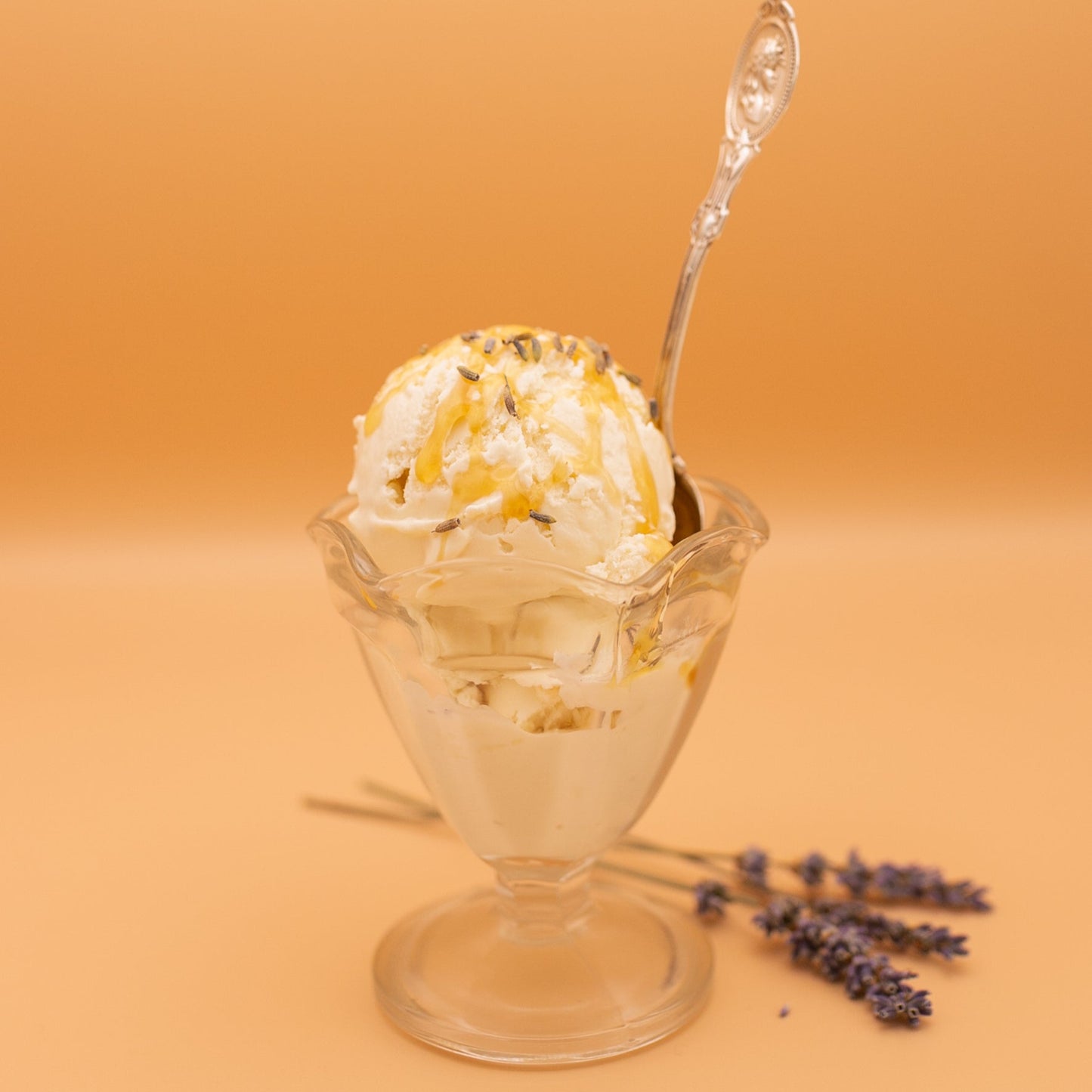Glass sundae dish with ice cream and lavender flowers on a peach background