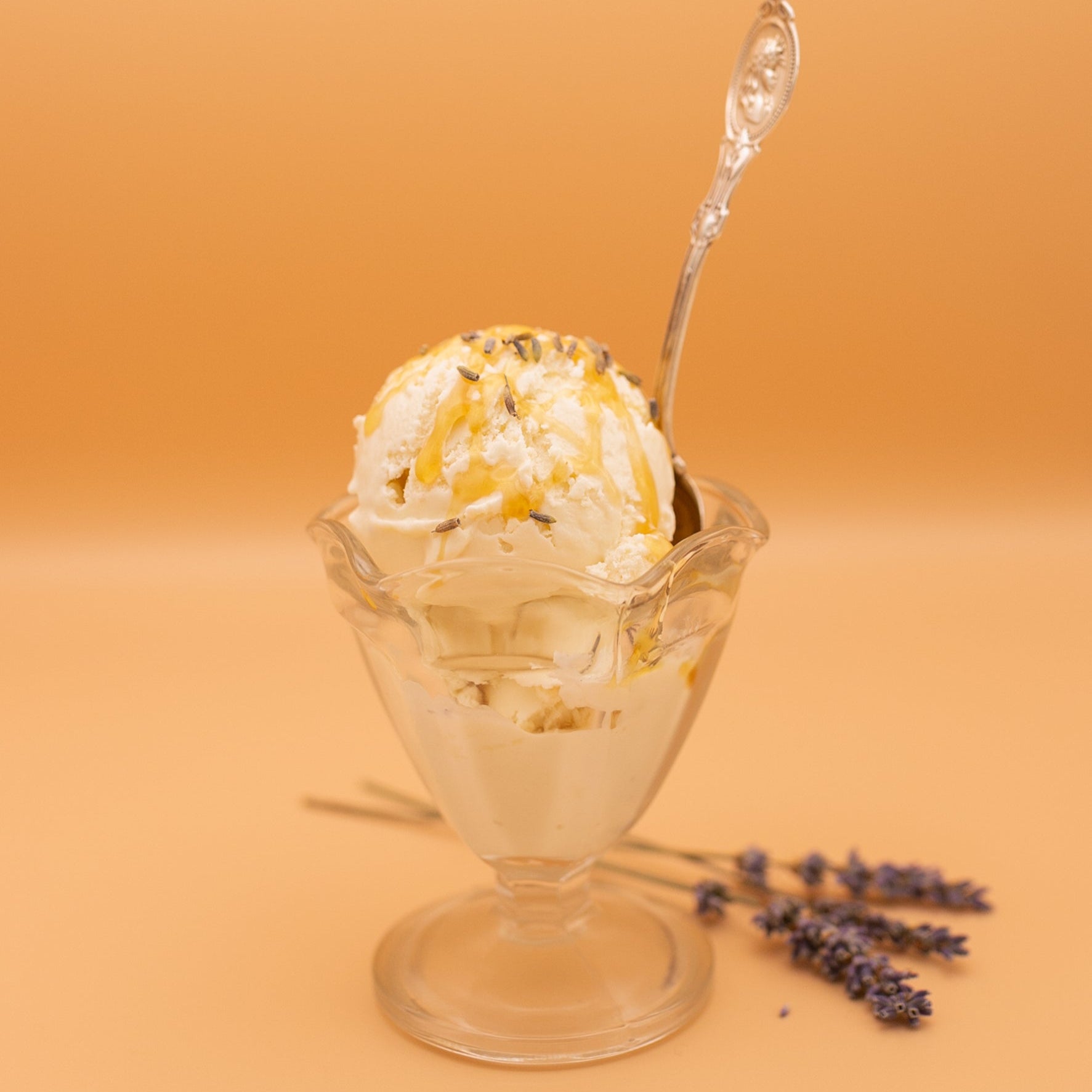 Glass sundae dish with ice cream and lavender flowers on a peach background