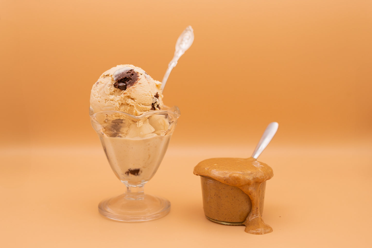 Ice cream with a spoon in a glass bowl next to a container of ice cream on an orange background