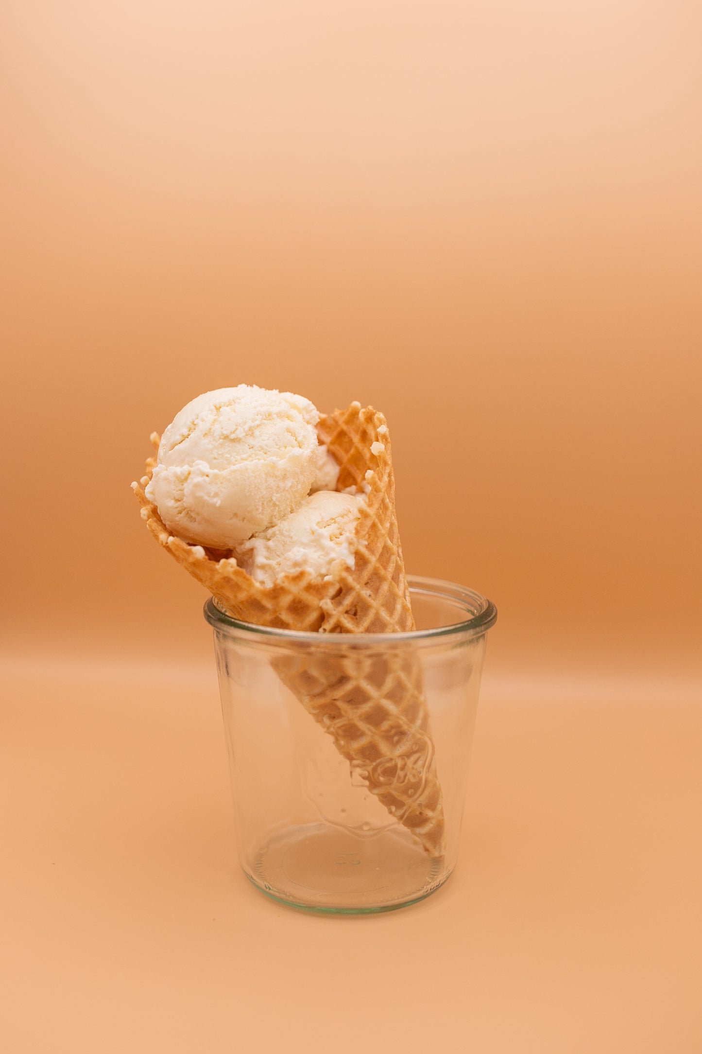 Ice cream cone with two scoops of vanilla ice cream in a glass container on an orange background