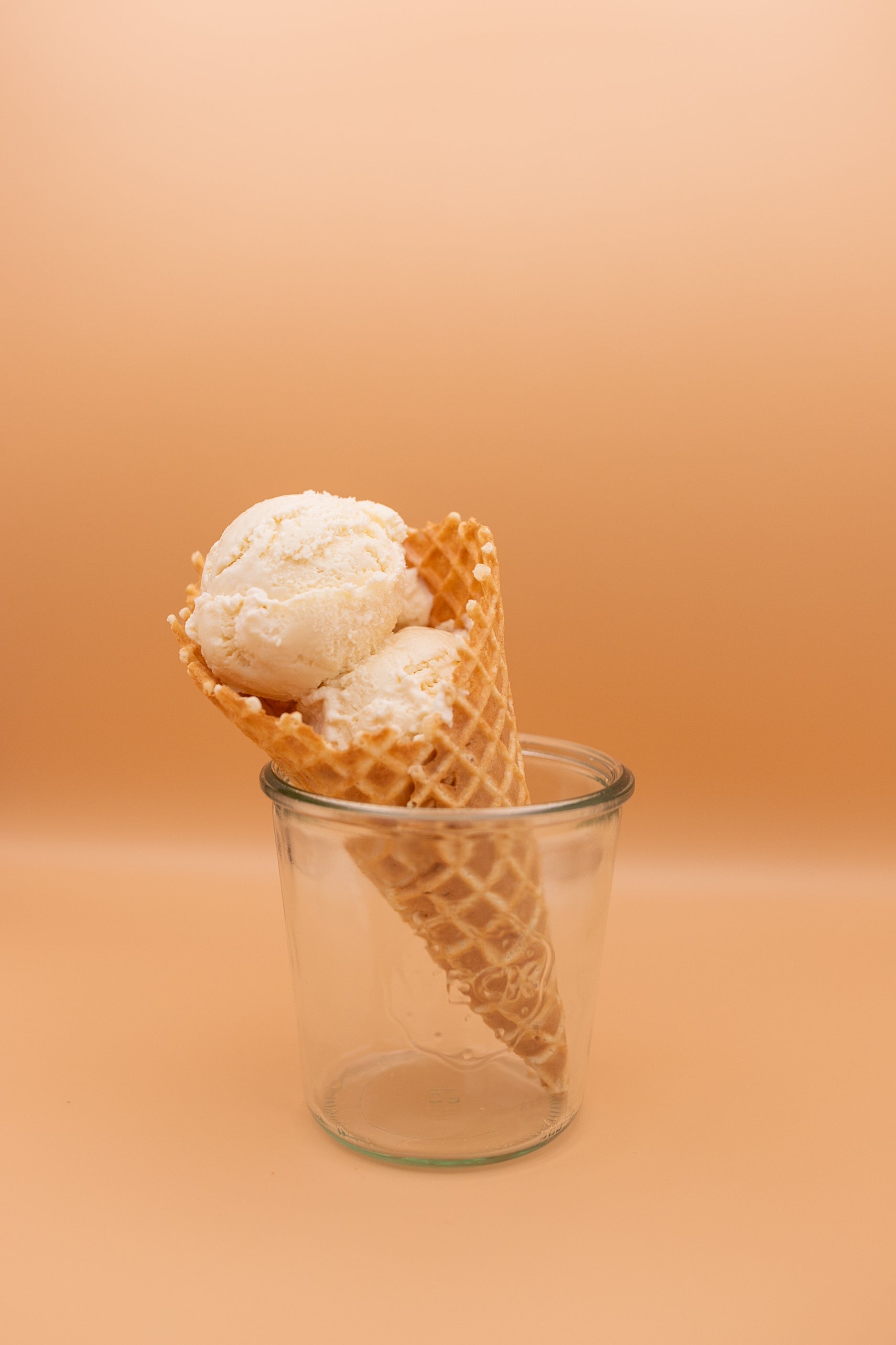 Ice cream cone with two scoops of vanilla ice cream in a glass container on an orange background